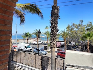 Une rue côtière bordée de voitures garées, de palmiers et offrant une vue sur la mer.
