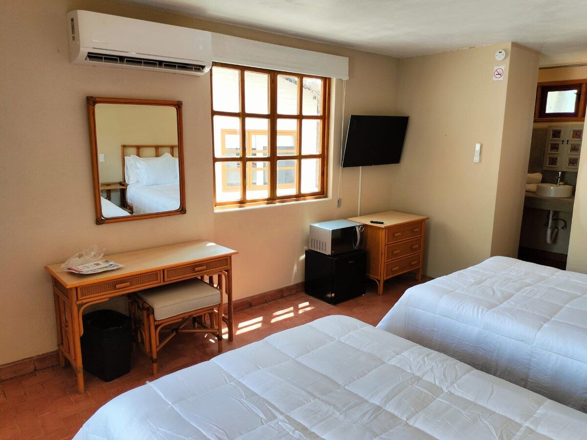 A hotel room with two beds, a desk, a television, and a window with blinds.