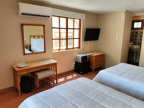 A hotel room with two beds, a desk, a television, and a window with blinds. - Sandy Shores 3A (La Paz)
