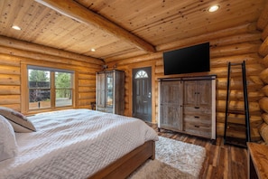 A log cabin bedroom with a bed, wardrobe, and a mounted TV.