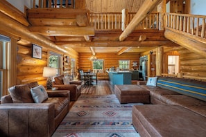 A log cabin interior with a living room, dining area, kitchen, and a staircase.