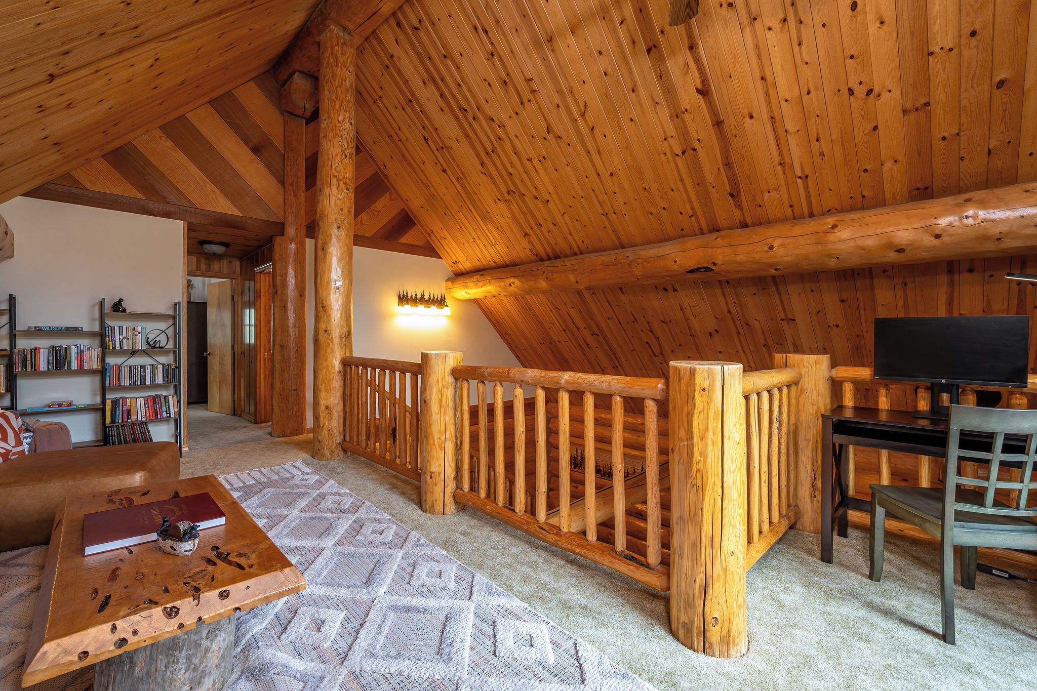 A cozy cabin interior with a wooden ceiling, a bookshelf, a fireplace, and a television.