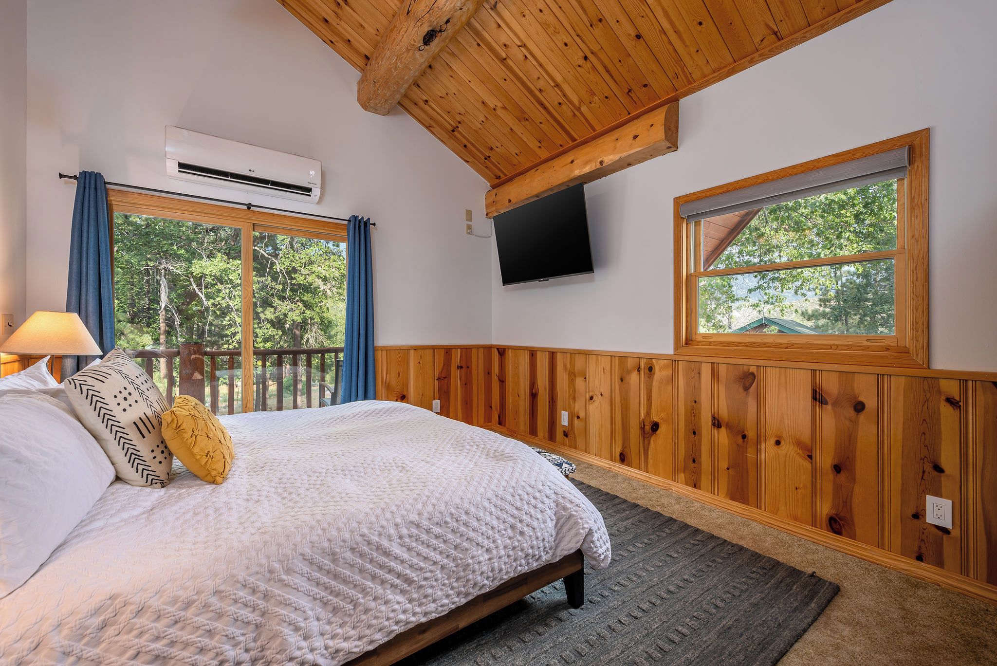 A bedroom with a bed, a TV mounted on the wall, and a window with a view of trees.