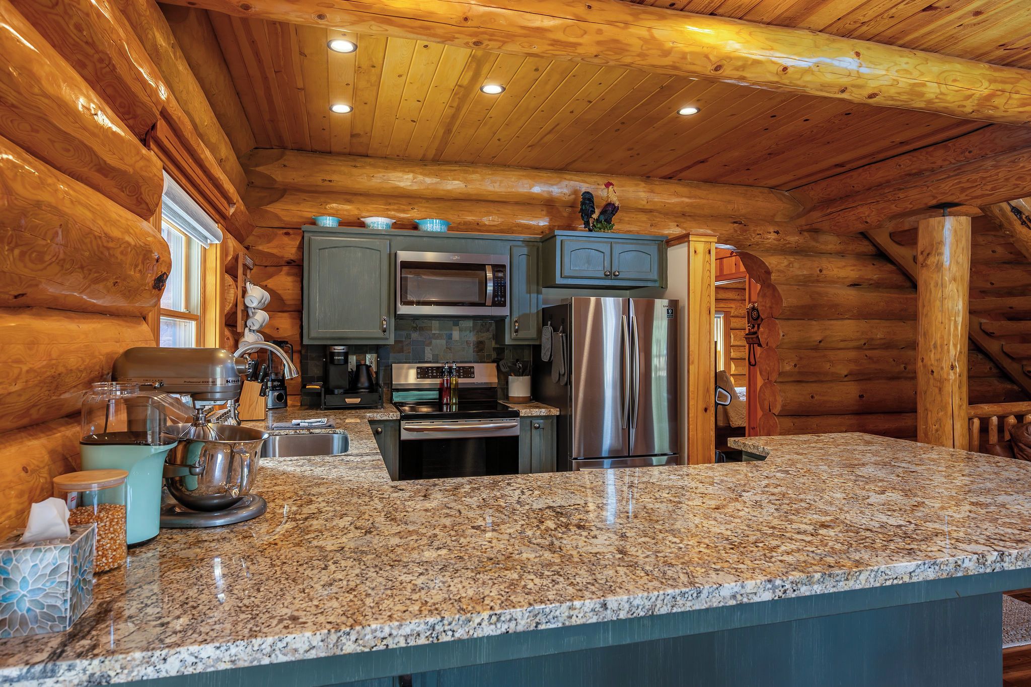 A log cabin kitchen with granite countertops, stainless steel appliances, and wooden walls.