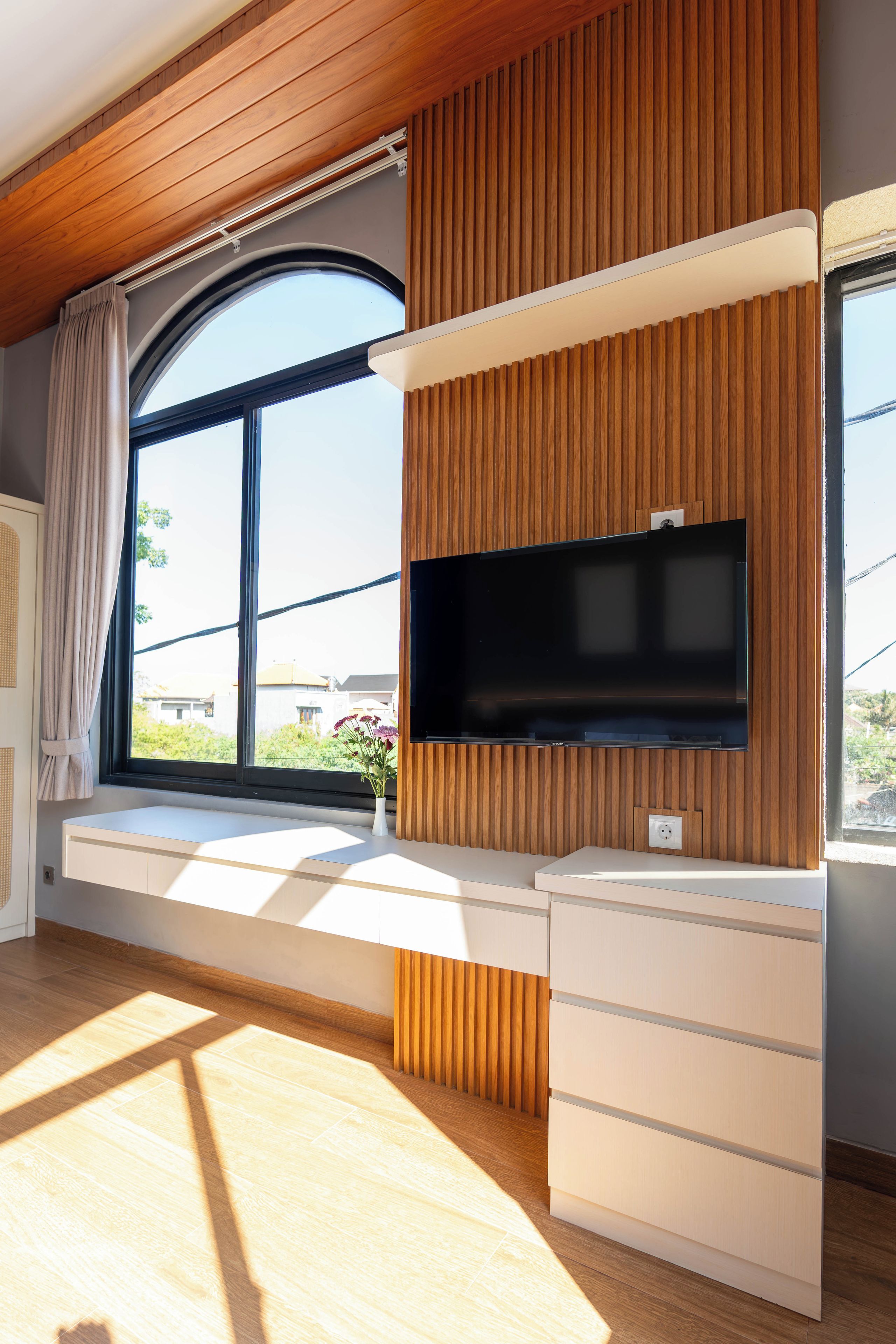 A modern room with a built-in TV, wooden paneling, a window with a view, and a built-in desk.