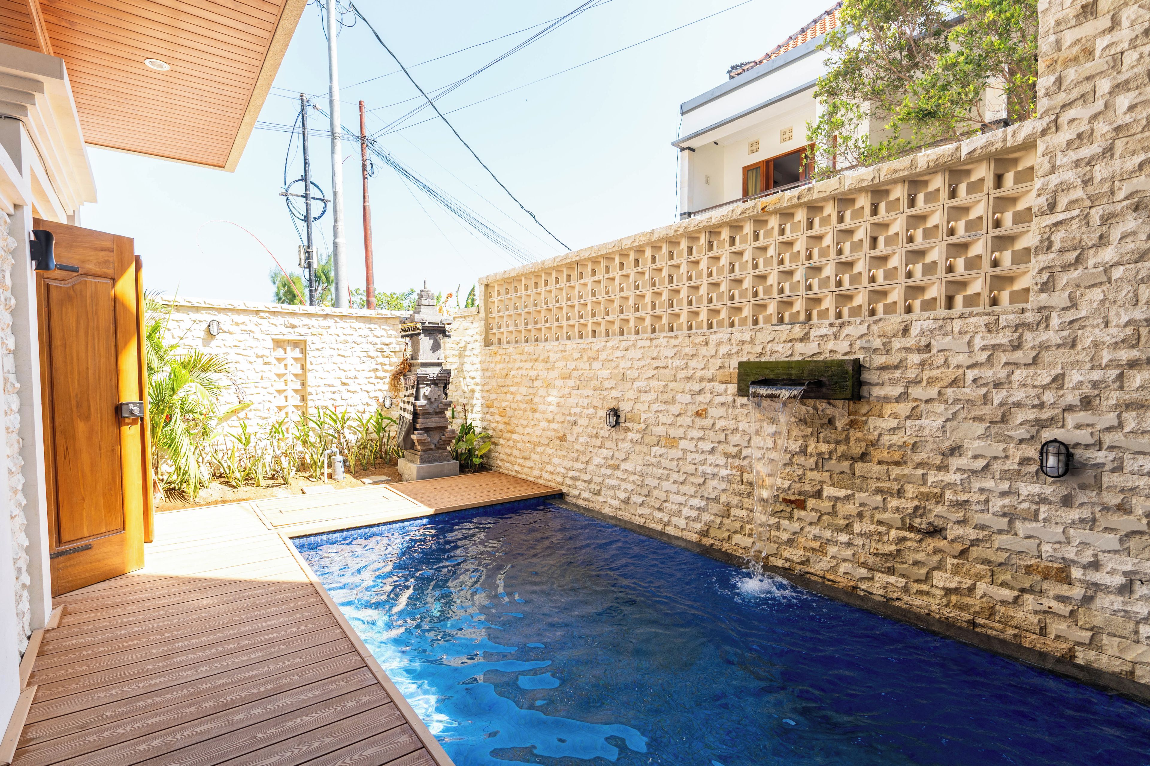 A swimming pool with a wooden deck, a stone wall, and a small garden area.