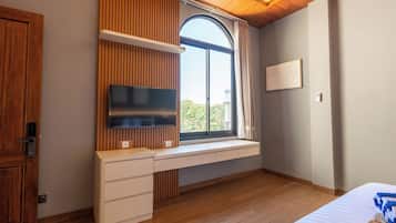 A bedroom with a built-in desk, a television, a window with curtains, and a bed with a patterned blanket.