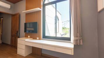 A modern room with a built-in desk, a flat-screen TV, and a large window with curtains.