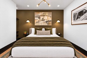 A hotel room with a large bed, a painting on the wall, and two wall-mounted lamps. - All Suites Six Bedroom (New Orleans)