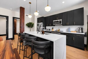 A modern kitchen with a central island, black cabinets, stainless steel appliances, and bar stools. - All Suites Six Bedroom (New Orleans)