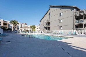 Un espace piscine comprenant des chaises longues, un belvédère et un immeuble à plusieurs étages doté de balcons.