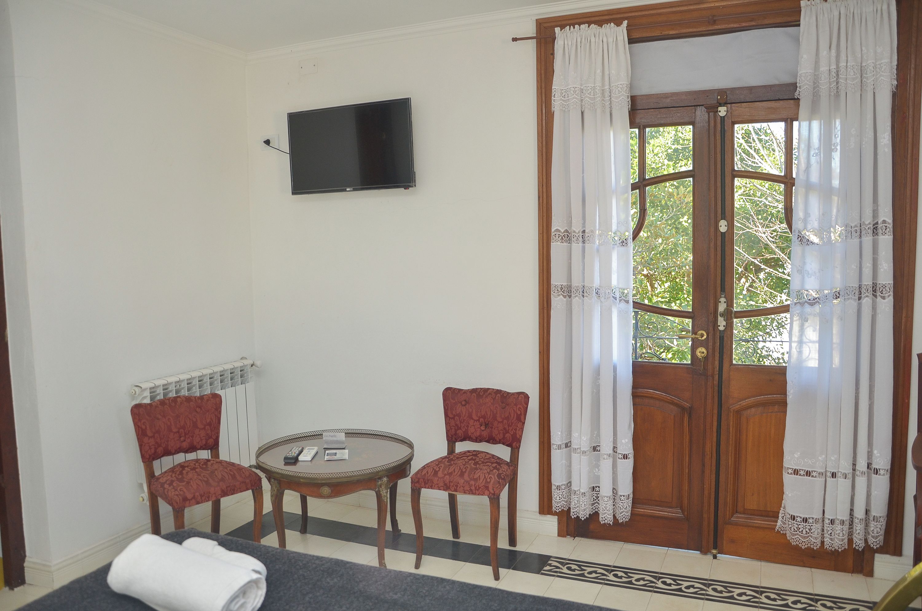 A room with a television mounted on the wall, two chairs, a small table, and a door with curtains.