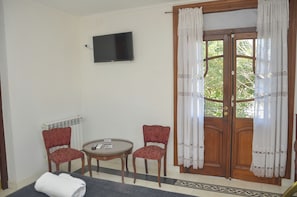 Une pièce avec un téléviseur fixé au mur, deux chaises, une petite table et une porte avec des rideaux.