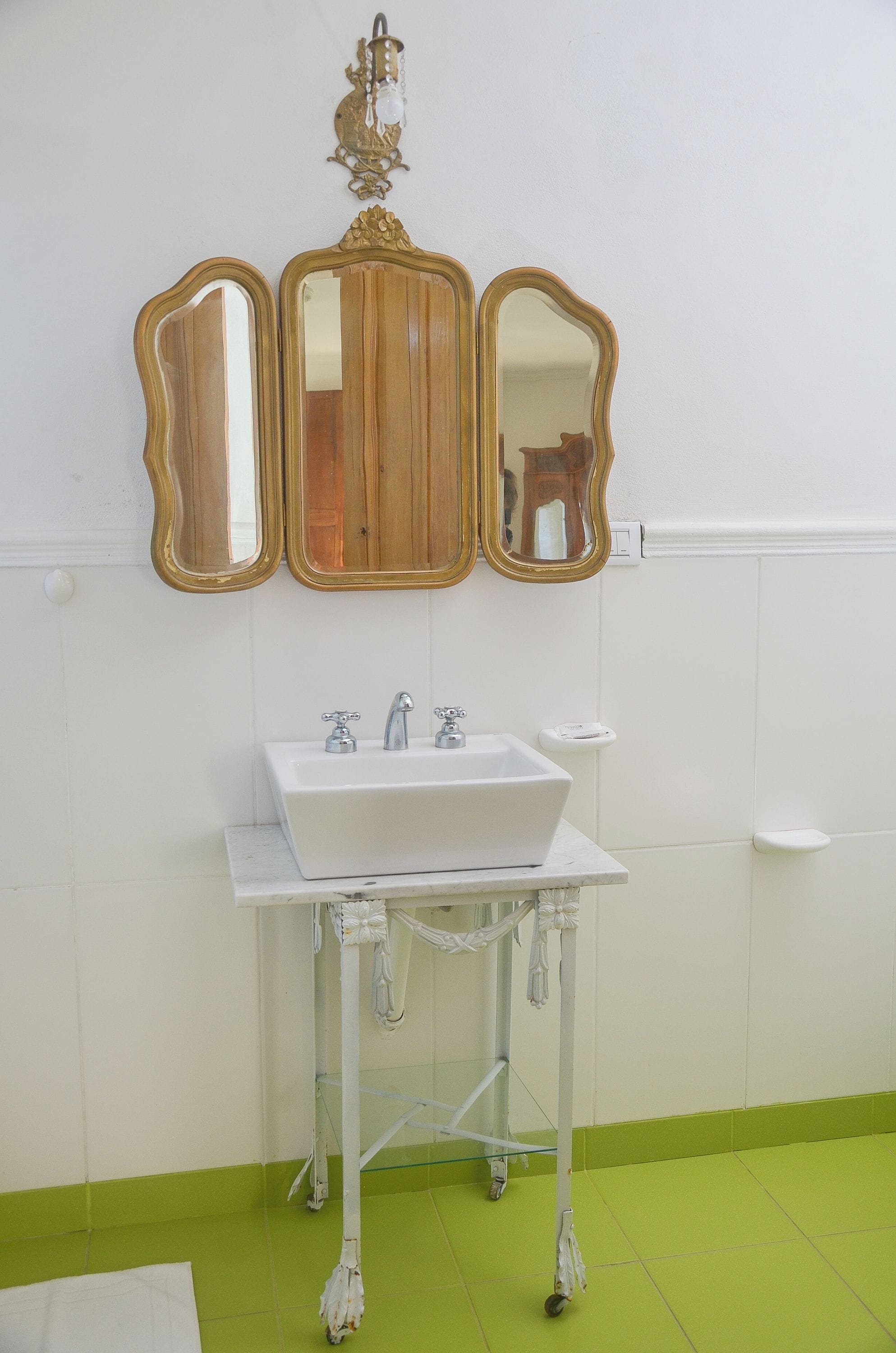 Un baño con un lavabo blanco, tres espejos y un suelo verde.