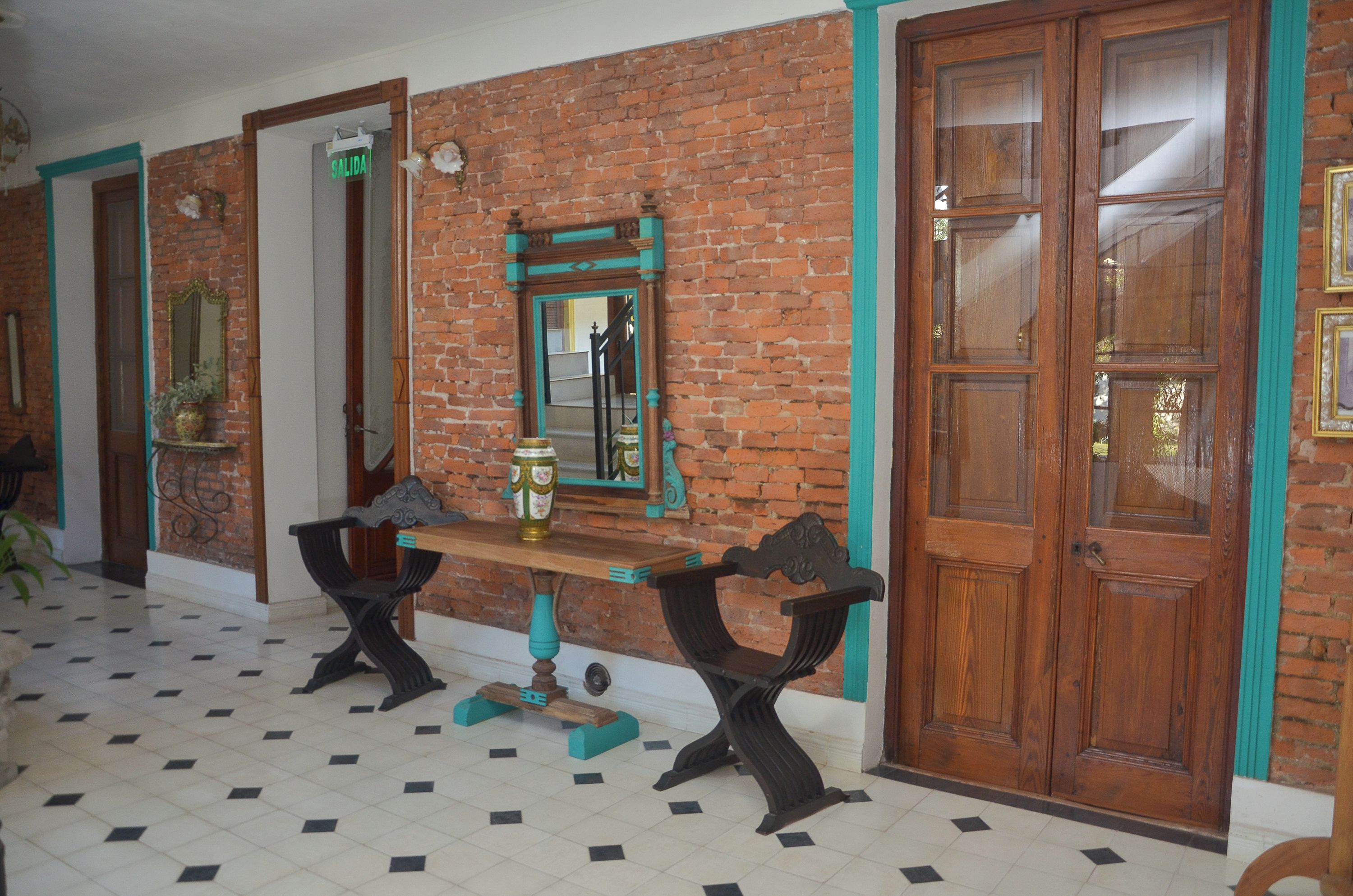 Una habitación con pared de ladrillo, puerta de madera, espejo y una mesa con sillas.
