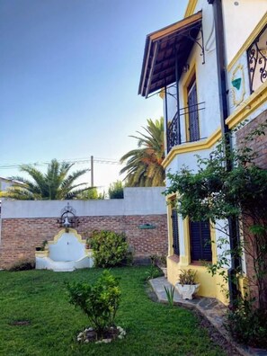 A two-story building with a balcony, a fountain, and a well-maintained garden. - Posada Los Angelos (Ramallo)