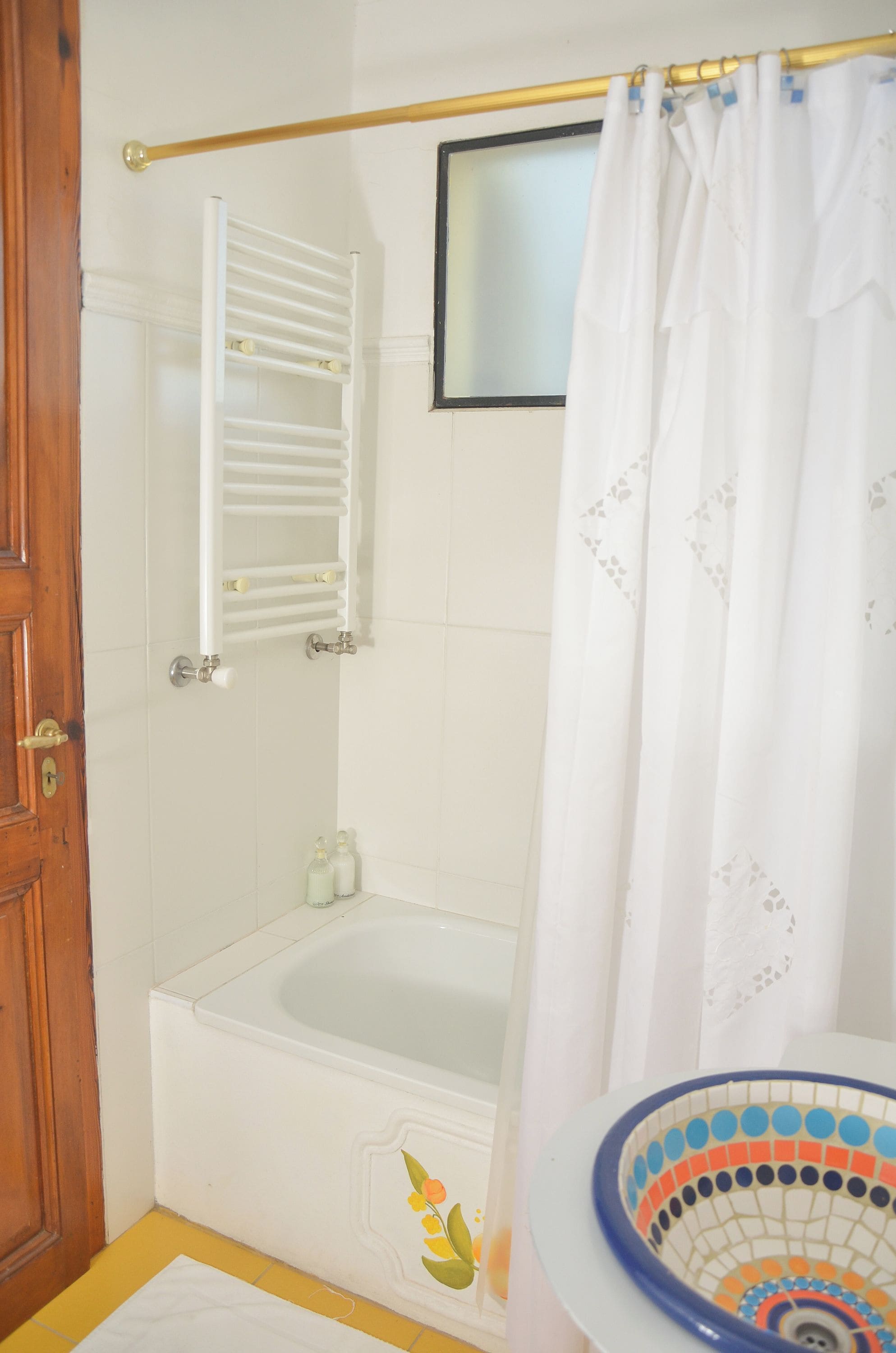 A bathroom with a bathtub, a shower curtain, a towel rack, and a toilet with a colorful bowl.