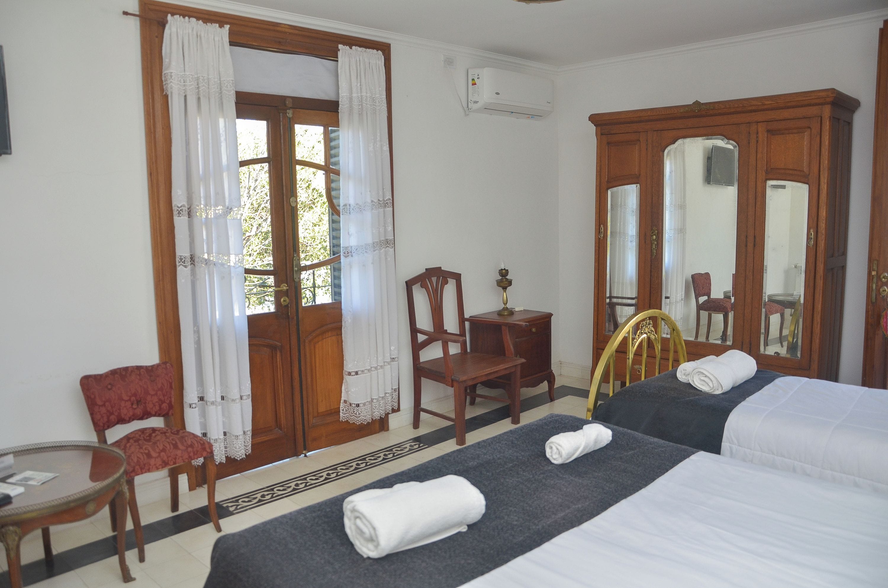 Une chambre d’hôtel avec deux lits, un bureau, une chaise, un miroir et une porte avec des rideaux.