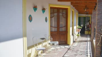 A covered outdoor area with a wooden door, a tiled floor, and a metal chair.