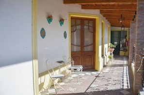 A covered outdoor area with a wooden door, a tiled floor, and a metal chair. - Posada Los Angelos (Ramallo)