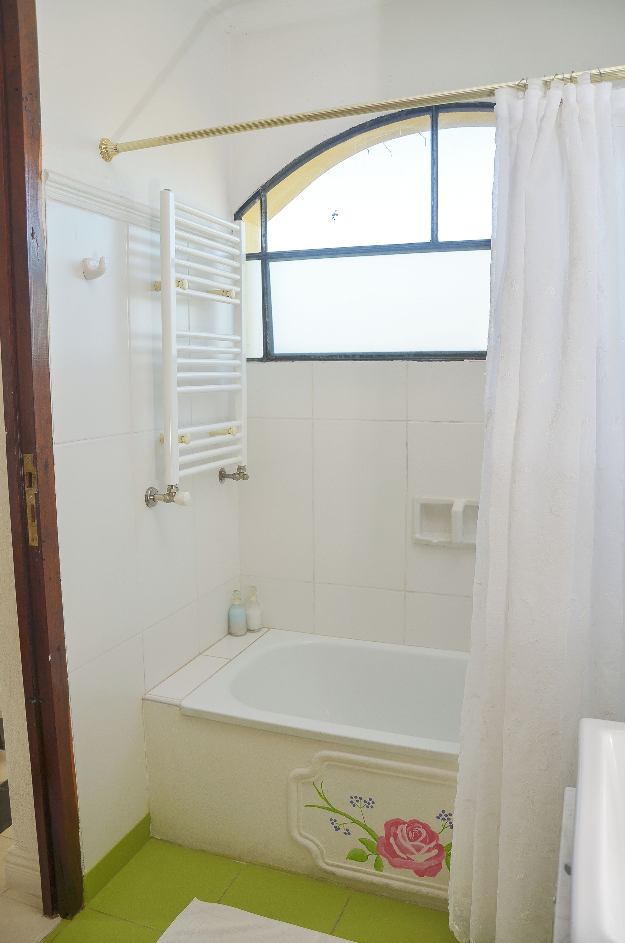 Un baño con bañera, una ventana con marco azul, un perchero blanco y un suelo verde.