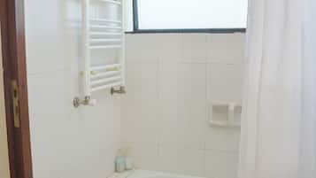 Un baño con bañera, una ventana con marco azul, un perchero blanco y un suelo verde.