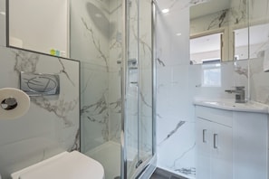 A modern bathroom with a glass-enclosed shower, a white toilet, and a marble-tiled vanity. - Sutherland Apartments - Apt 41 (London)