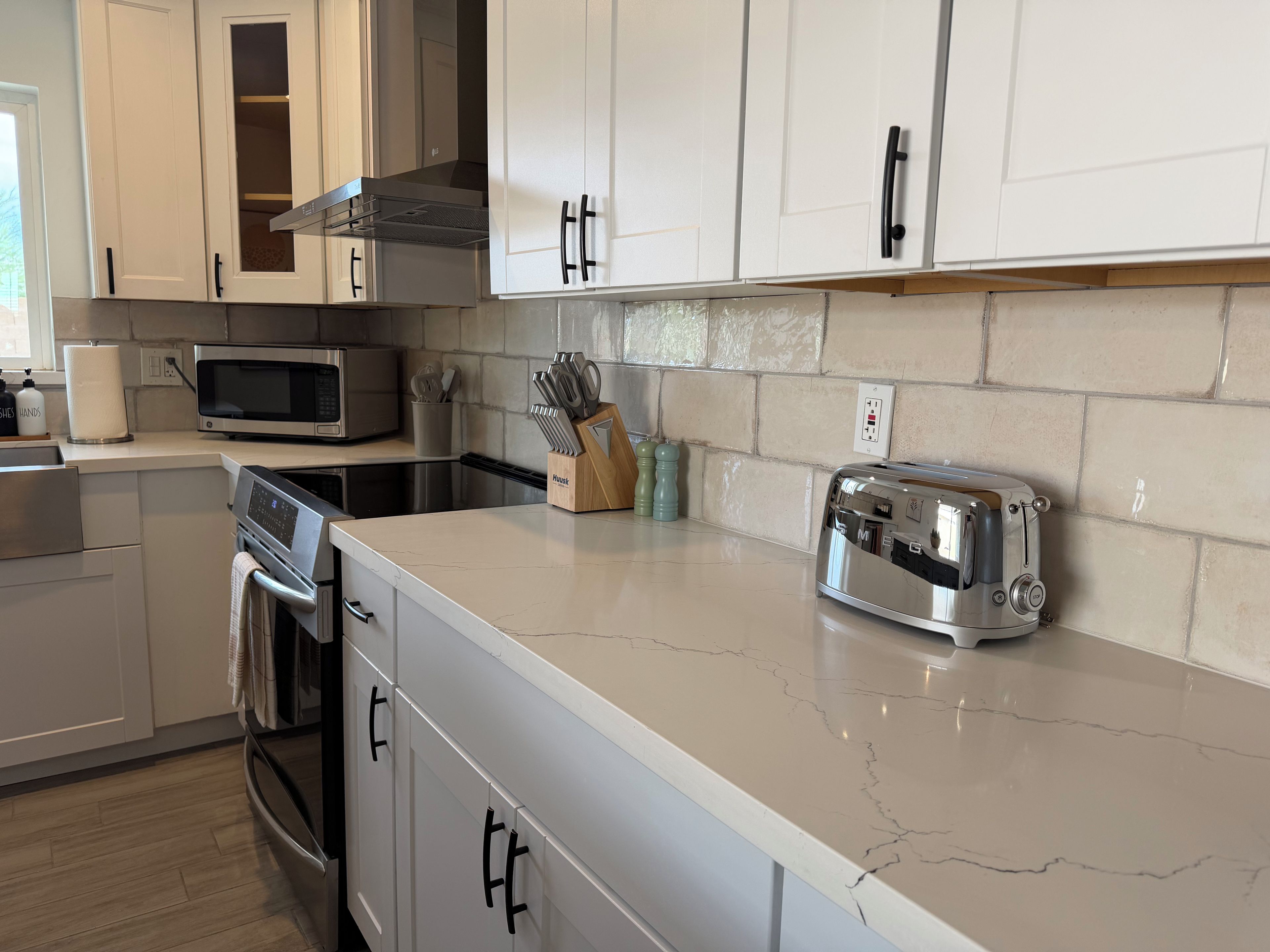 A kitchen with white cabinets, a stainless steel microwave, a toaster, and a wooden utensil holder.