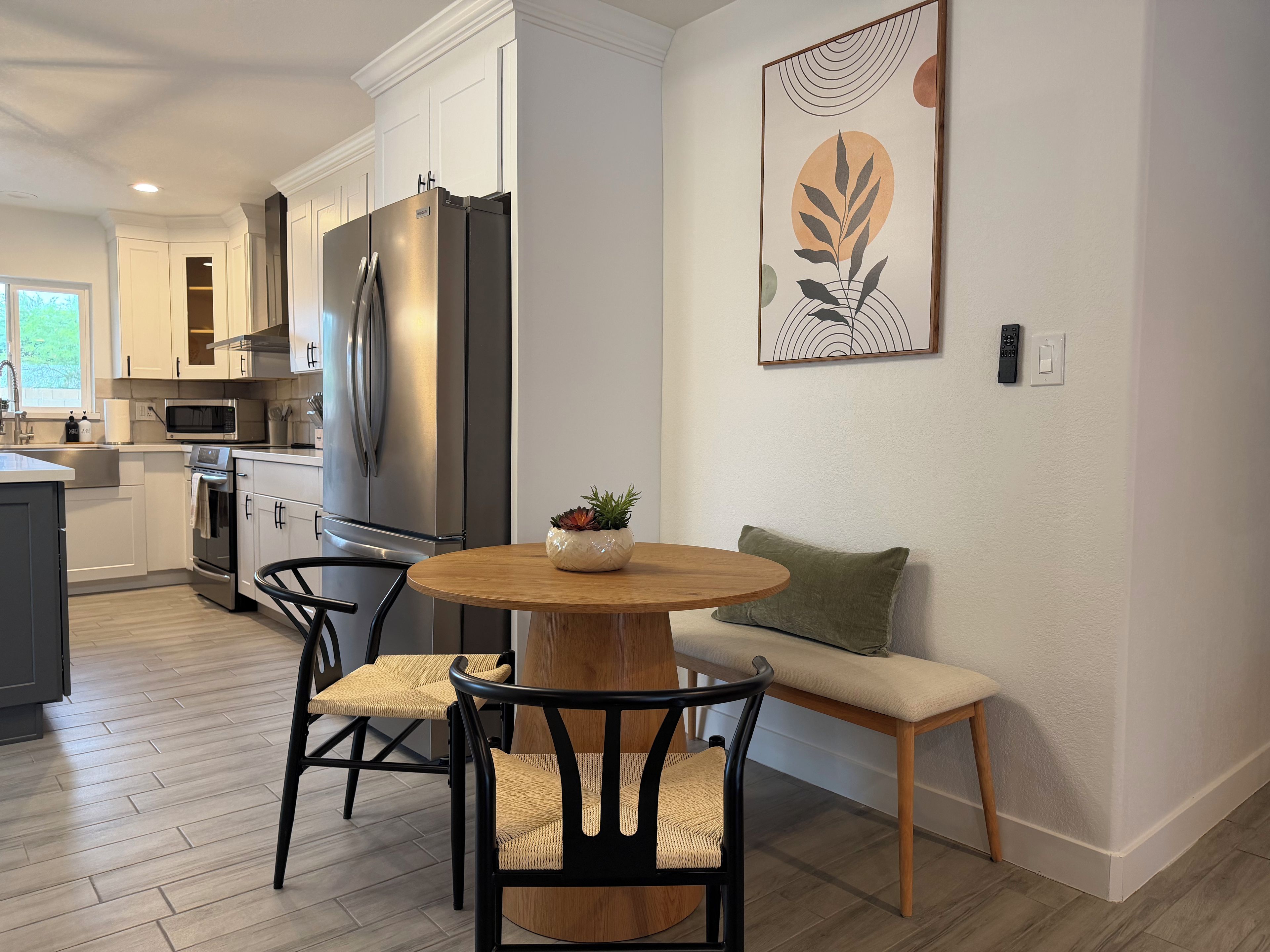 A modern kitchen with stainless steel appliances, a dining area with a round wooden table, and a wall-mounted artwork.