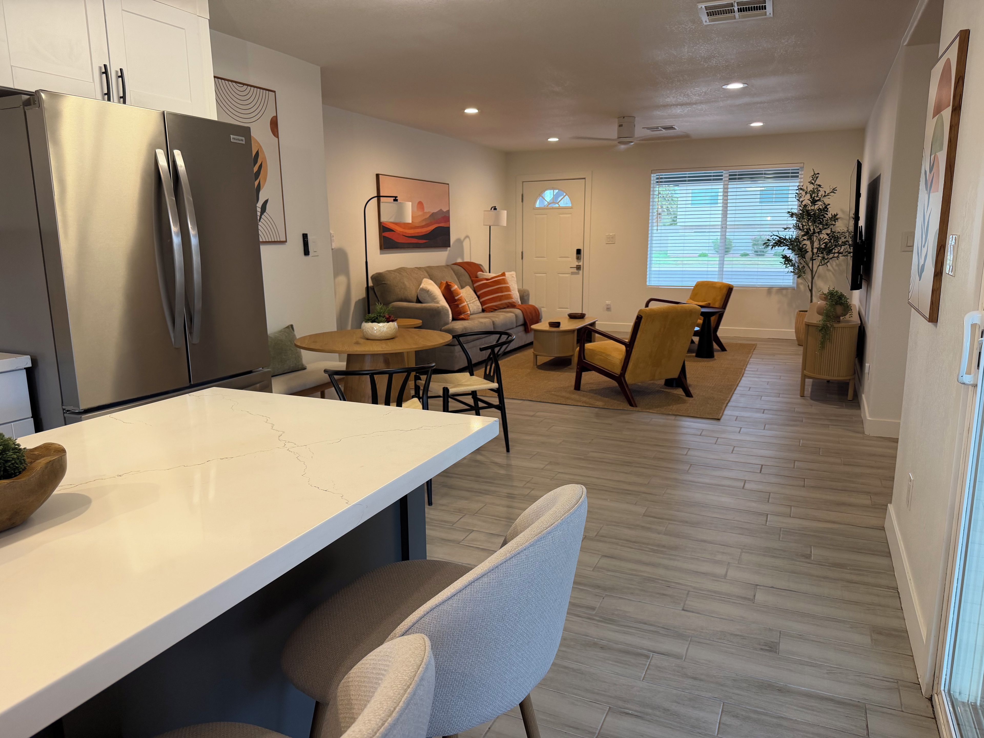 A modern kitchen with a dining area, wooden flooring, and a view to the living room.