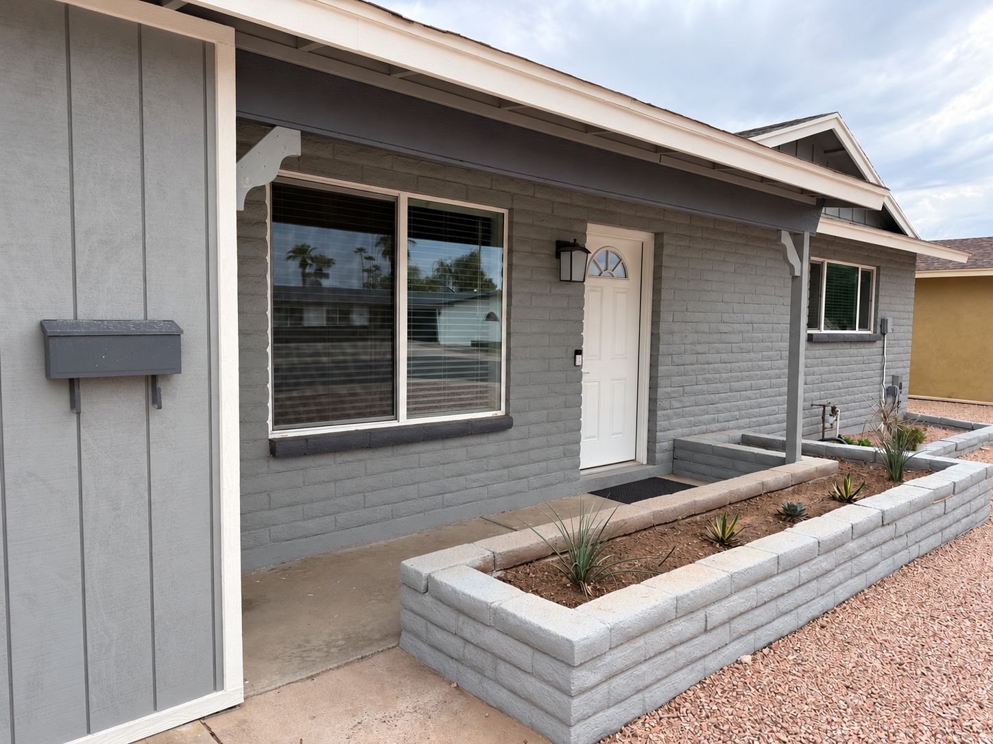 A residential house with a grey exterior, a white front door, and a small front yard with a planter.