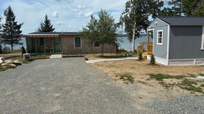 A gravel driveway leading to a cabin with a wooden deck and a small shed. - Union Bay Cottages - The Prefix (Trenton)