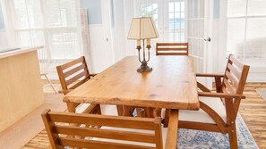 Een houten eettafel met vier stoelen, een lamp en uitzicht op zee door grote ramen.