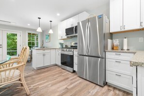 A modern kitchen with white cabinetry, stainless steel appliances, and a wooden floor. - Seaberry Woods A Nature-filled Retreat Near Camden (Hope)
