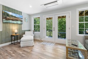 Ein Zimmer mit Bett, Schreibtisch, Stuhl, einem Gemälde und großen Fenstern mit Blick auf Bäume.