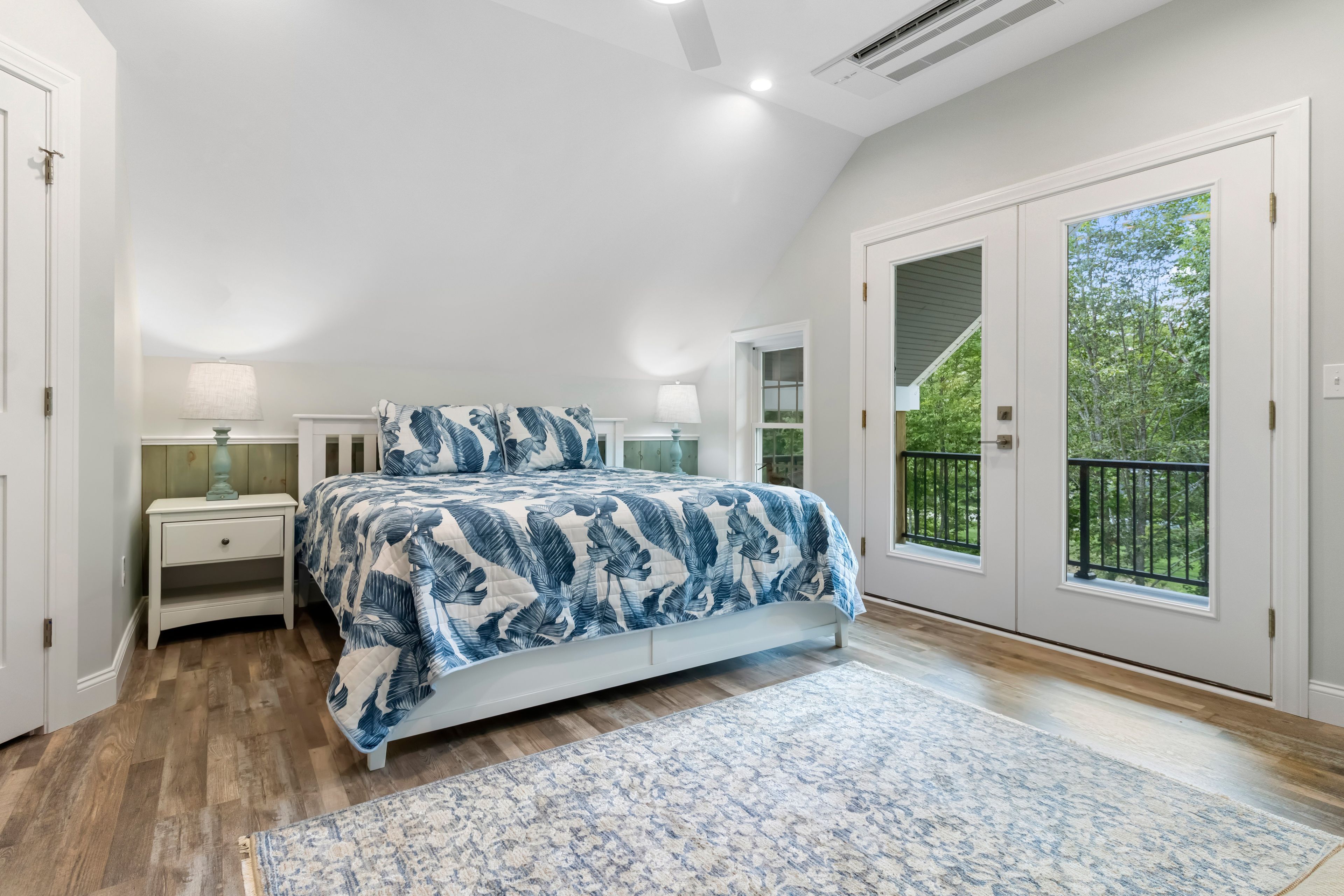 A bedroom with a large bed, a nightstand, a dresser, and a window with a view of greenery.
