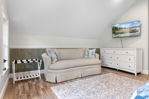 Ein Schlafzimmer mit einer Couch, einem Schminktisch, einem Fernseher und Holzboden.