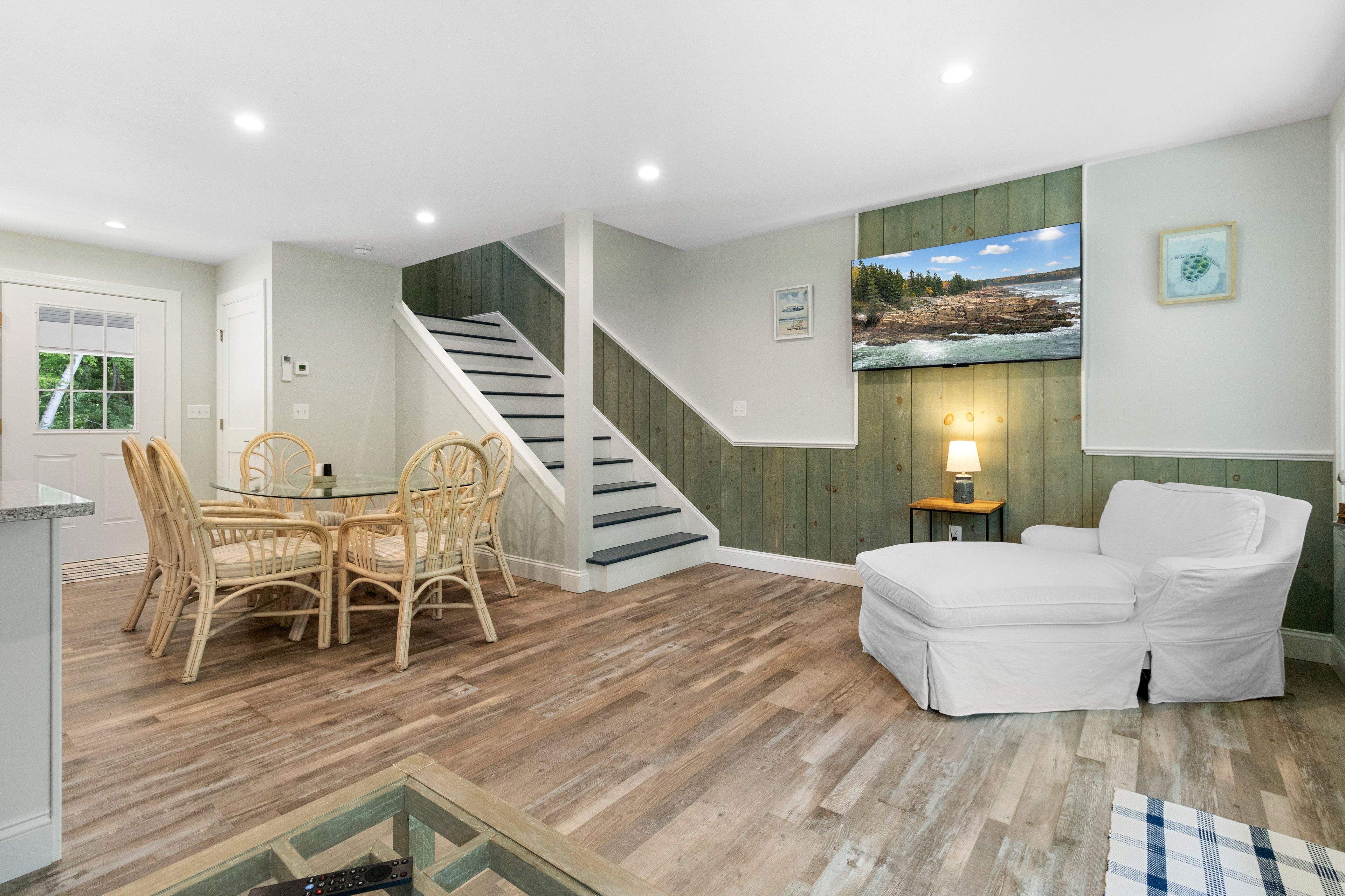 A spacious living area with a dining table, chairs, a sofa, a staircase, and a television mounted on the wall.
