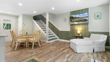 A spacious living area with a dining table, chairs, a sofa, a staircase, and a television mounted on the wall.