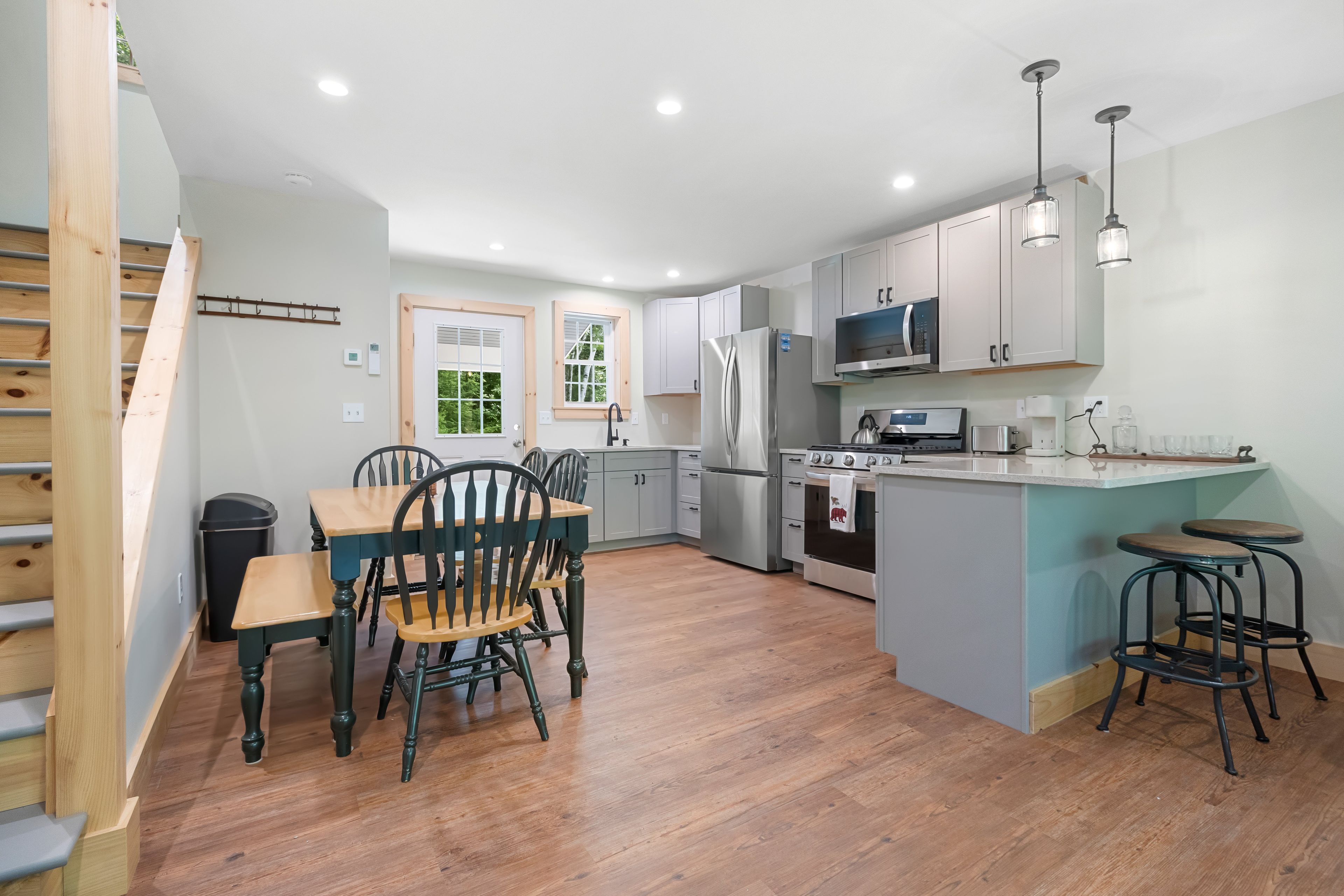 A modern kitchen with wooden flooring, a dining area with chairs, a refrigerator, a microwave, and a stove.