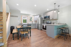 A modern kitchen with wooden flooring, a dining area with chairs, a refrigerator, a microwave, and a stove. - Blackberry Woods A Peaceful Maine Retreat in Hope (Hope)