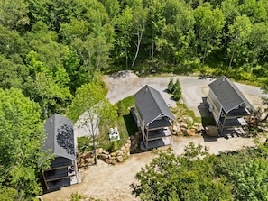Ein abgelegenes Chaletgebiet mit drei Chalets, umgeben von dichtem Wald, mit einem Schotterweg und einer kleinen Lichtung.