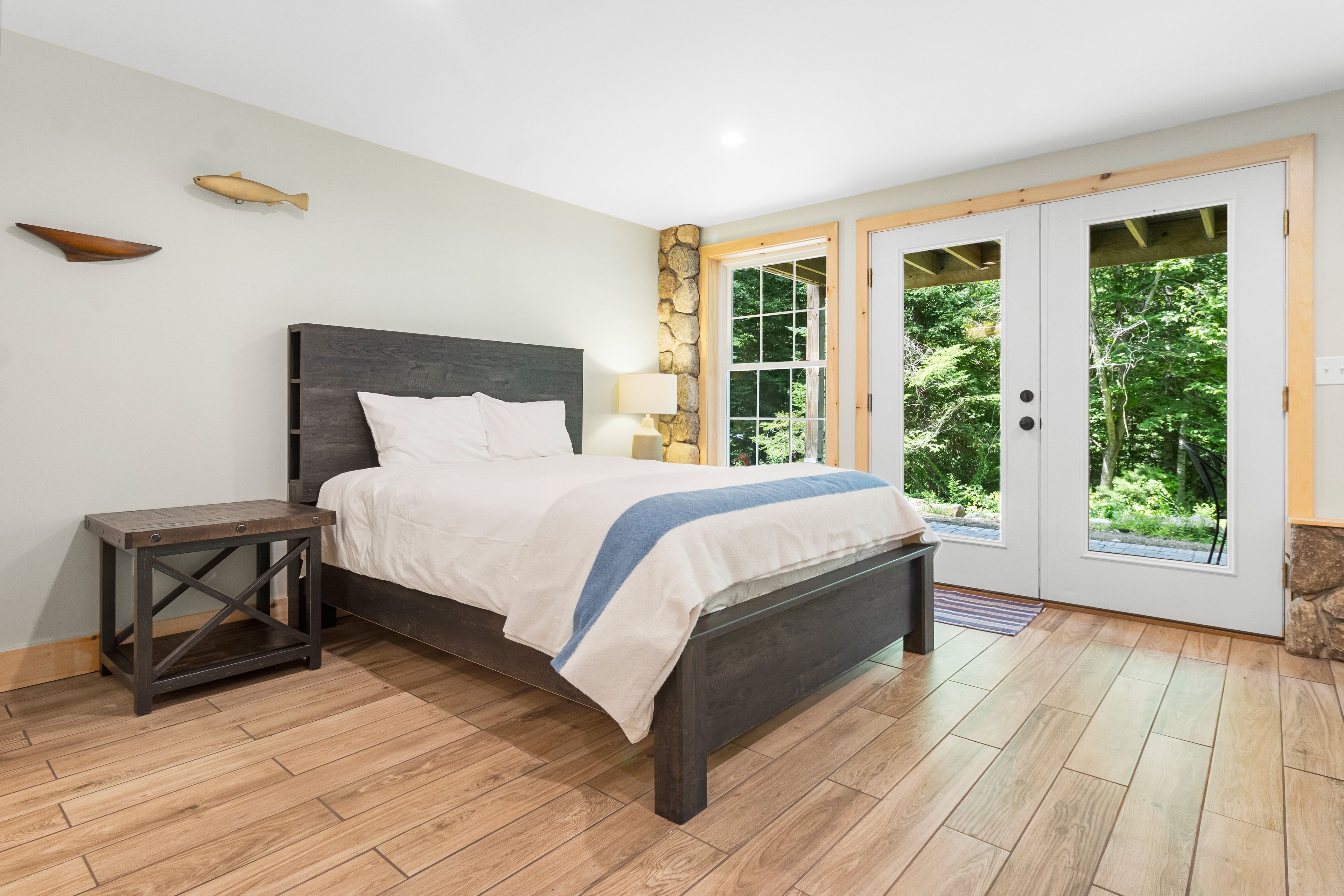 A bedroom with a bed, a nightstand, a stone wall, and a door leading to a garden.