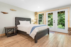 Ein Schlafzimmer mit einem Bett, einem Nachttisch, einer Steinwand und einer Tür zu einem Garten.