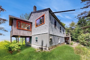 A two-story house with a wooden deck, a chimney, and a small porch. - Water View Home With Scenic Balcony, Grill, Board Games, and AC (Phippsburg)