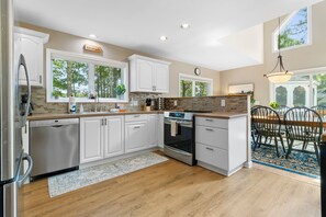 A modern kitchen with white cabinets, a Bosch dishwasher, a built-in oven, and a dining area with a table and chairs. - Laurel Shores 3br/3ba Oceanfront Harpswell Retreat w/ Deck (Harpswell)