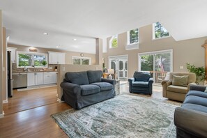 A spacious living area with a grey sofa, a patterned rug, and a dining area with a table and chairs. - Laurel Shores 3br/3ba Oceanfront Harpswell Retreat w/ Deck (Harpswell)