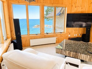Habitación con un ventanal grande con vista a una masa de agua, un sofá blanco, una mesa de vidrio y un televisor.
