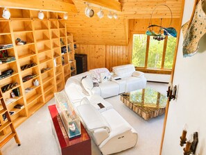 Interior acollidor d'una cabana amb una prestatgeria de fusta, un sofà blanc i una taula de cafè de vidre.
