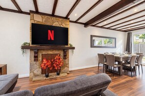 A modern living room with a stone fireplace, a flat-screen TV mounted above it, and a dining area with a table and chairs. - 4BR Wembley Stay w/ Pool Table & Free Parking (Greater London)